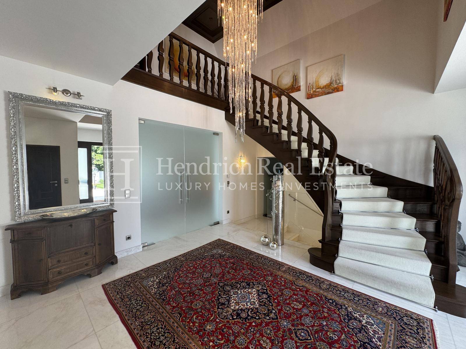 Geräumiger Eingangsbereich mit Marmorboden, eleganter Holztreppe und einem opulenten Kronleuchter.