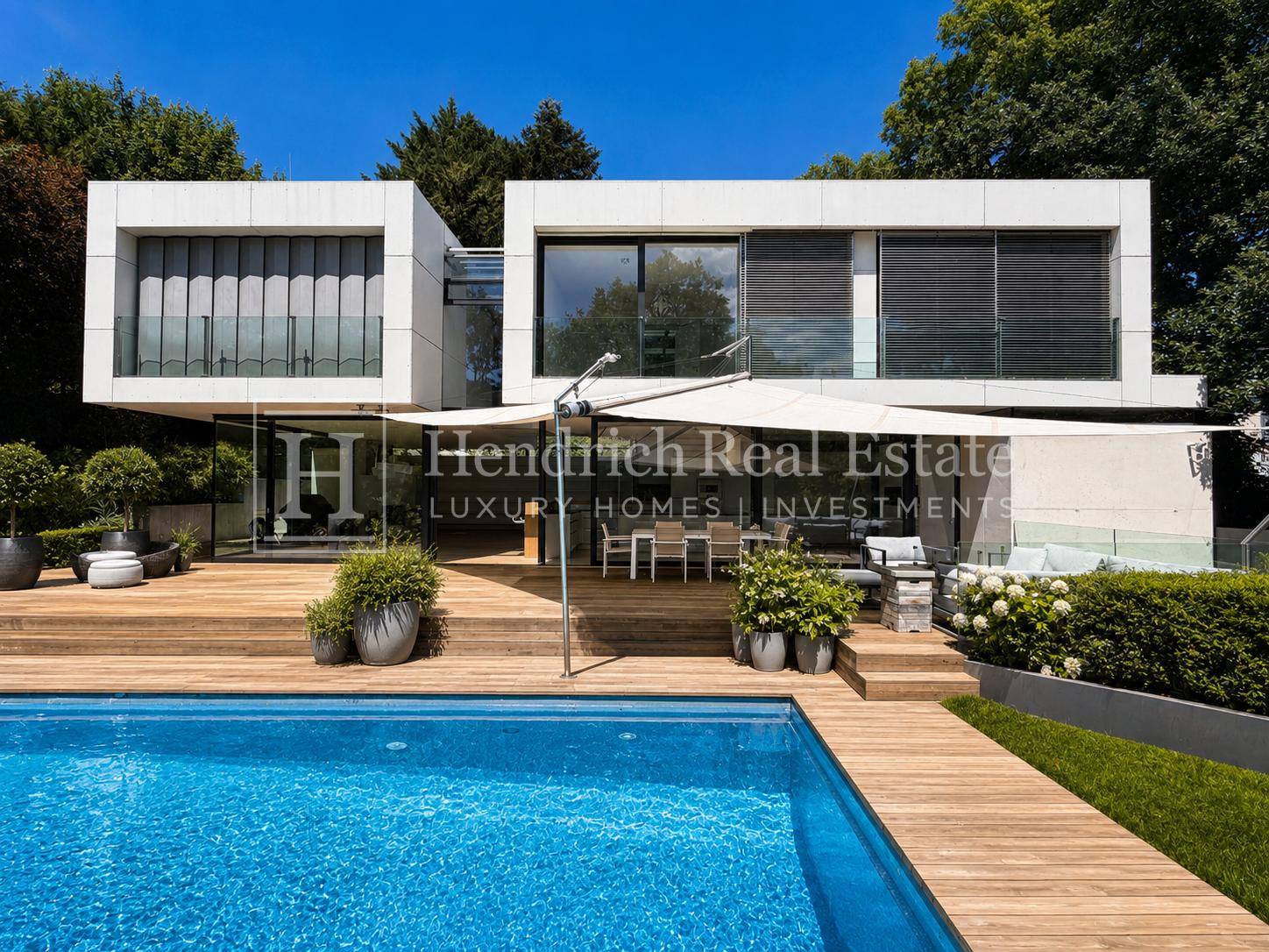 Luxuriöse Villa mit großem Pool, Holzdeck und Essbereich im Freien, umgeben von Grün.