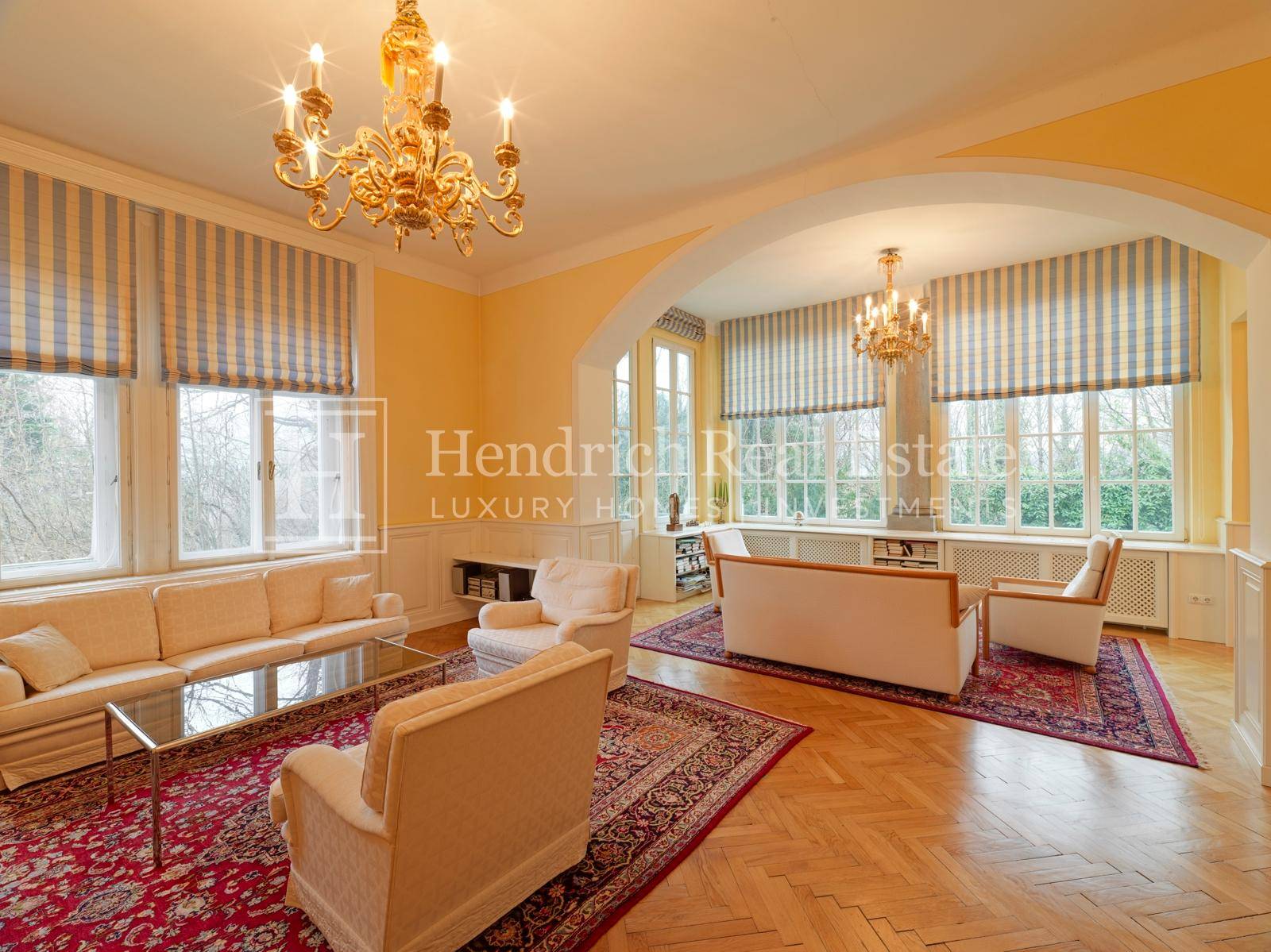 Geräumiges Wohnzimmer mit Fischgrätparkett, hohen Fenstern und zwei opulenten Kronleuchtern.