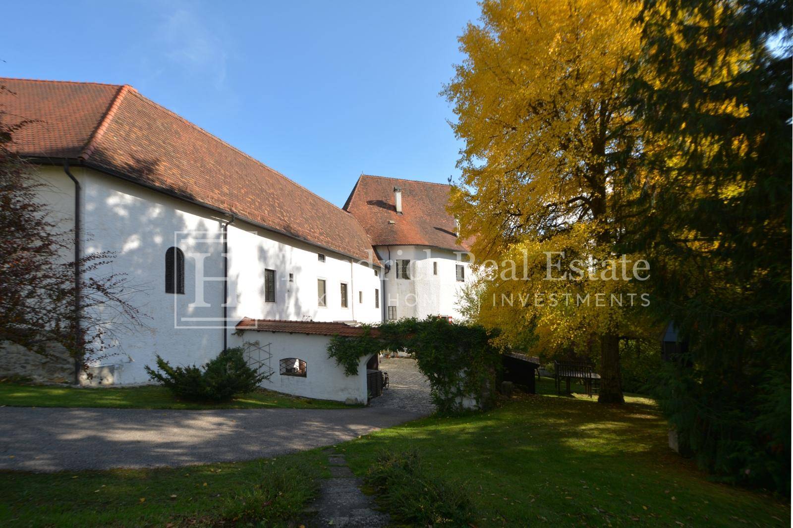 Seitenansicht des historischen Gebäudes mit weißer Fassade und Ziegeldach, umgeben von herbstlichen Bäumen.