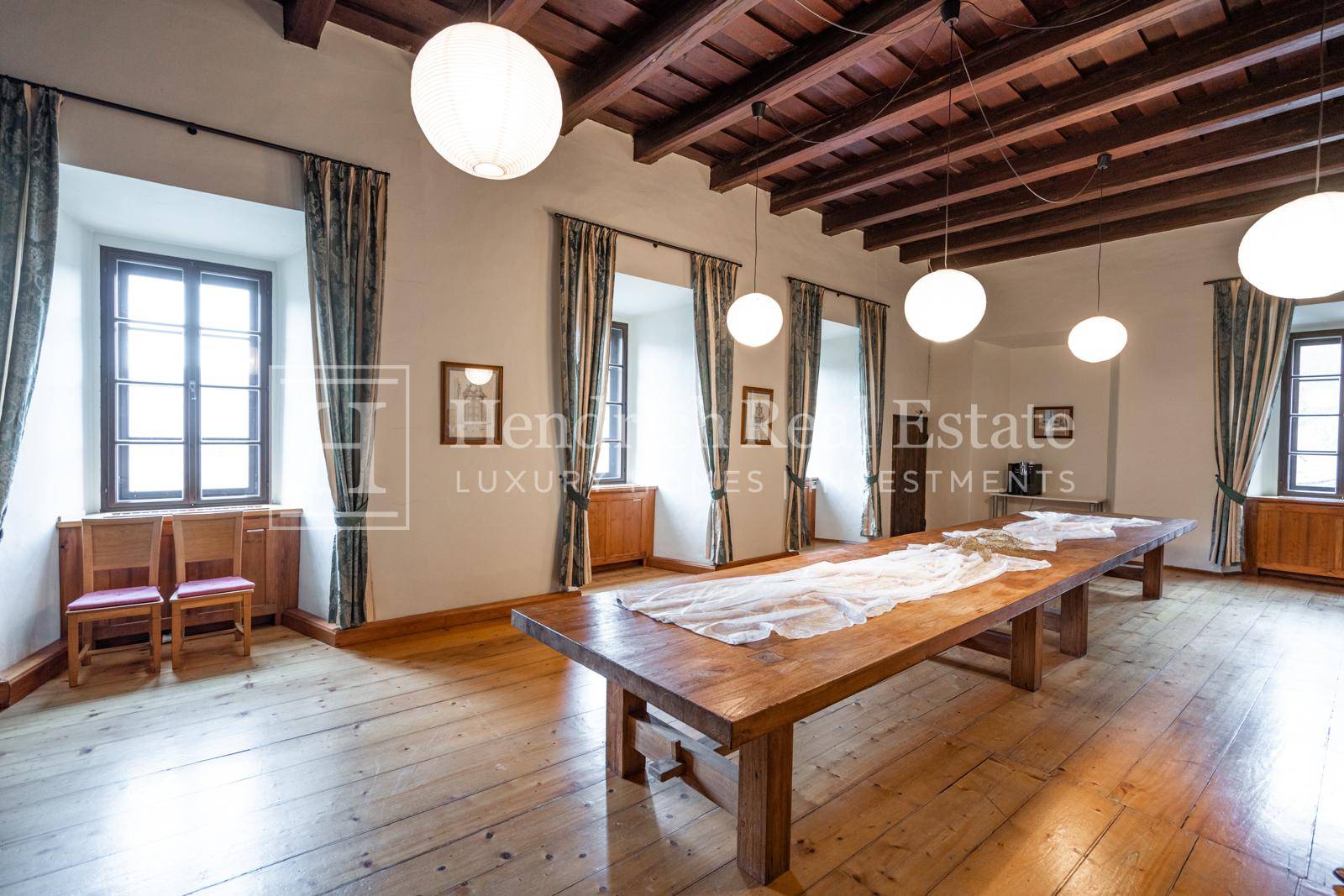 Geräumiger Saal mit langem Holztisch, Holzboden und sichtbaren Deckenbalken, ideal für große Versammlungen.