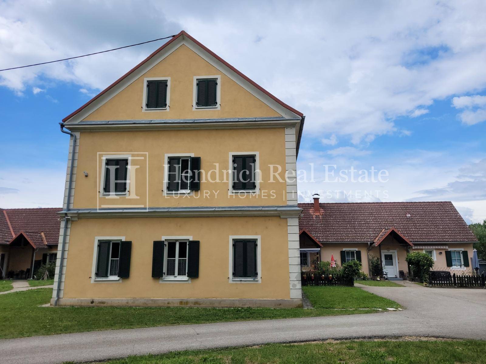 Vorderansicht eines historischen Gebäudes mit gelber Fassade und traditionellen grünen Fensterläden.