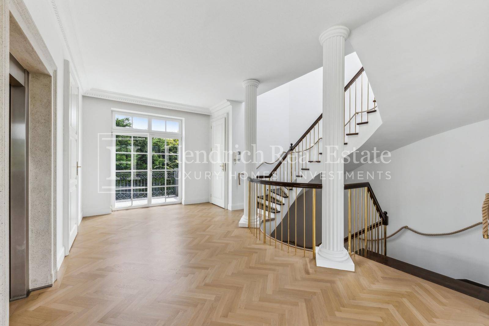 Repräsentativer Eingangsbereich mit eleganter Treppe, Säulen und einem modernen Aufzug.
