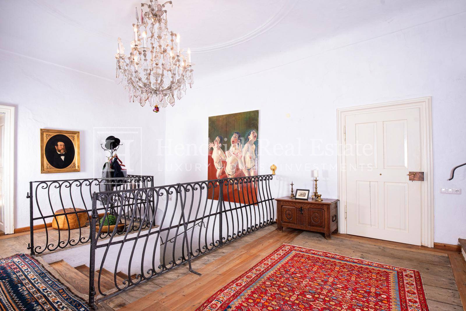 Eleganter Flur mit Holzboden, schmiedeeisernem Geländer und einem prächtigen Kronleuchter.