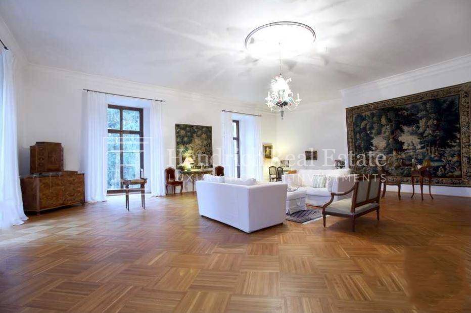Geräumiges Wohnzimmer mit elegantem Parkettboden, hohen Fenstern und klassischer Einrichtung, inklusive Kronleuchter.