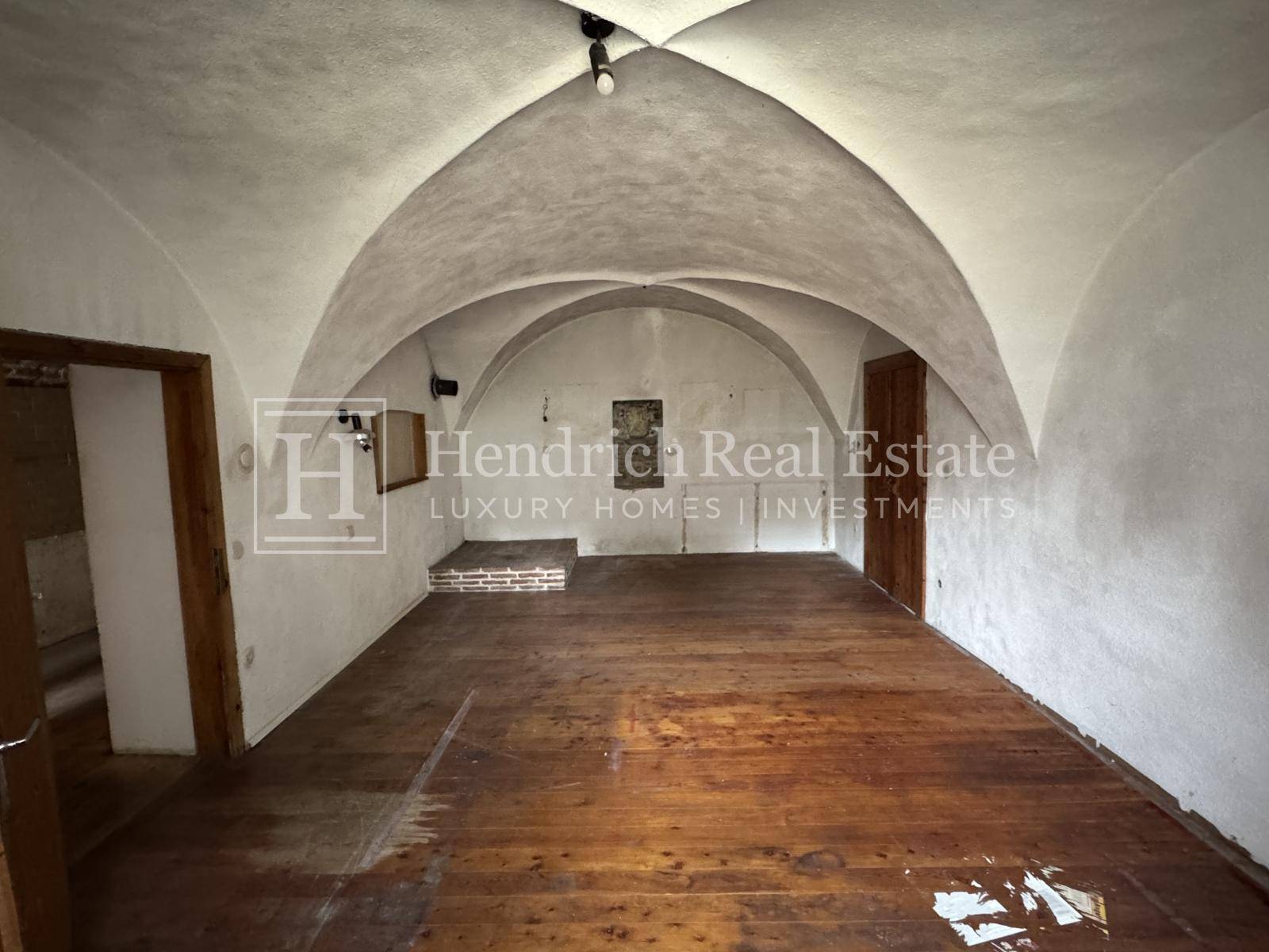 Großer Raum mit historischen Gewölbedecken und Holzdielenboden, ideal für eine Renovierung.