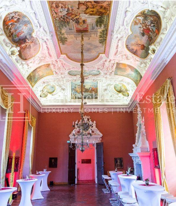 Prunkvoller Saal mit kunstvoll bemalter Decke, roten Wänden und einem imposanten Kronleuchter.