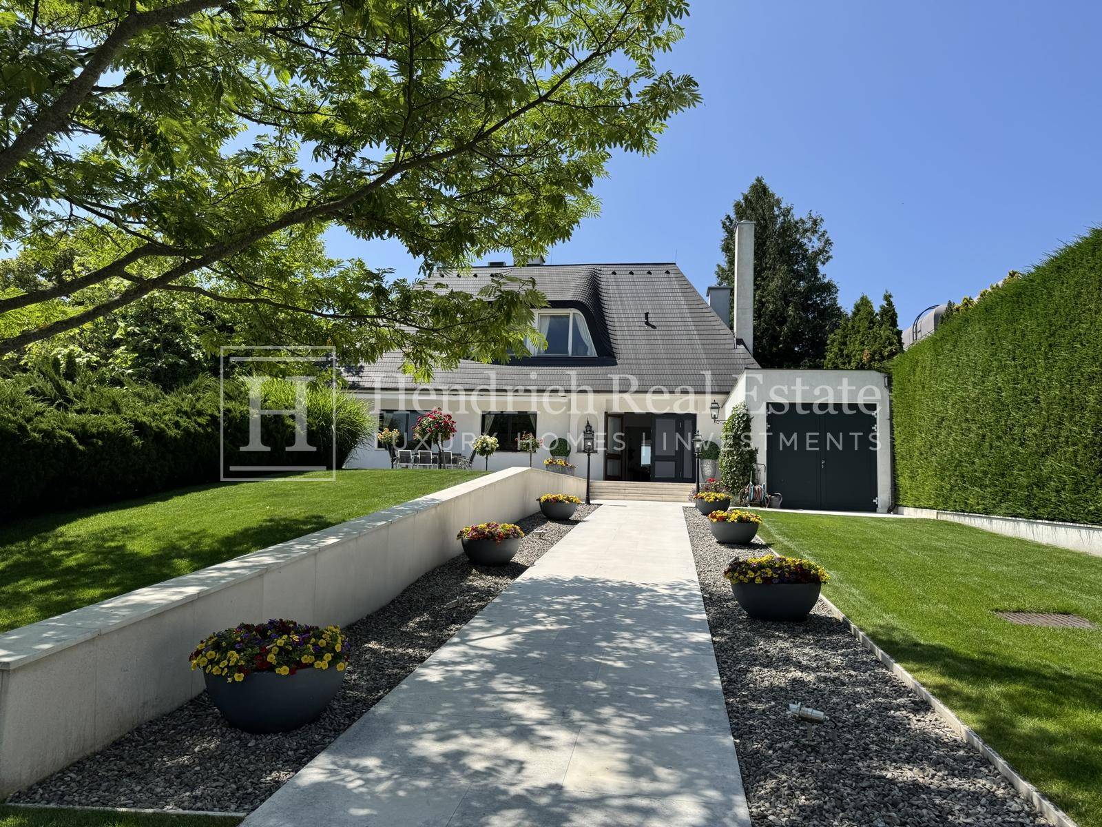 Eingangsbereich der modernen Villa mit gepflegtem Vorgarten, Zufahrt und dekorativen Pflanzkübeln.