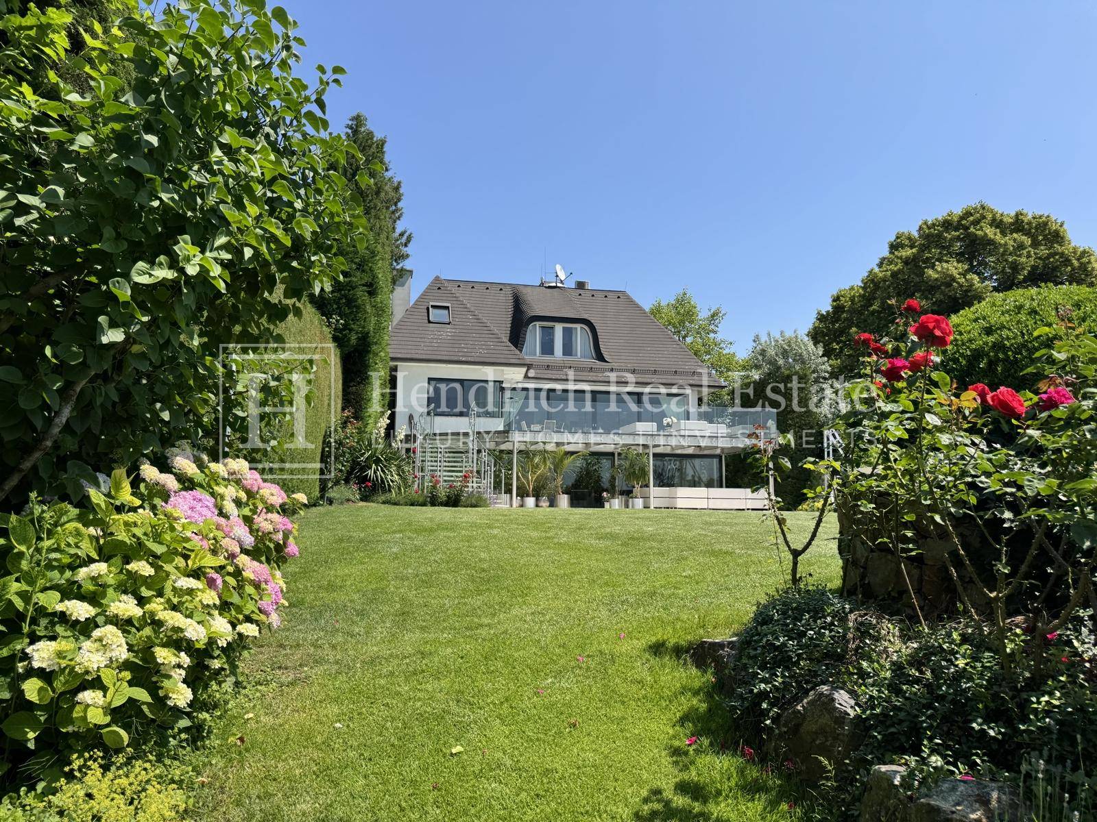 Elegante Villa mit weitläufigem Garten, blühenden Blumenbeeten und einer großen Terrasse.