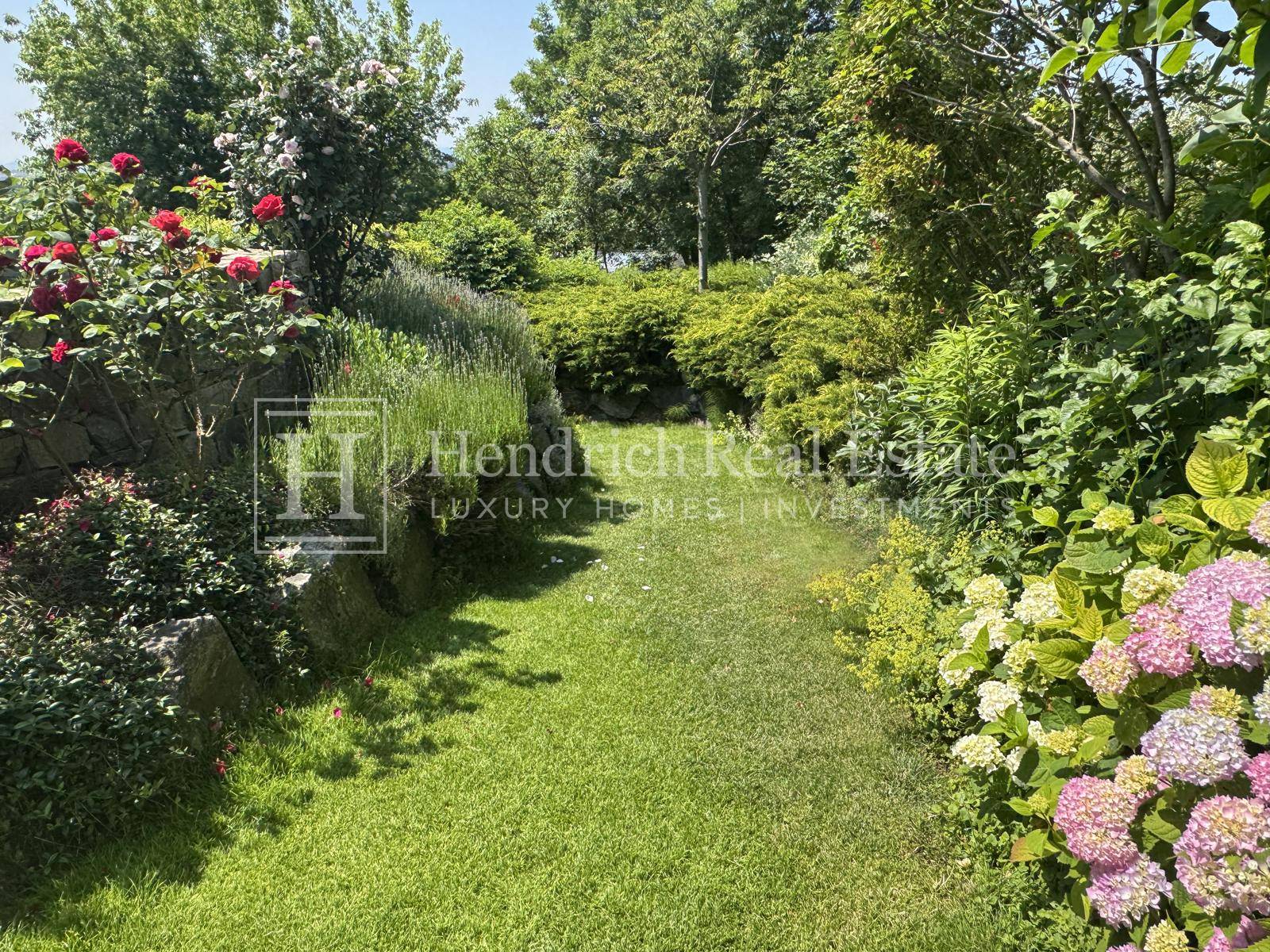 Idyllischer Gartenweg umgeben von üppigen Blumenbeeten und grünen Sträuchern an einem sonnigen Tag.
