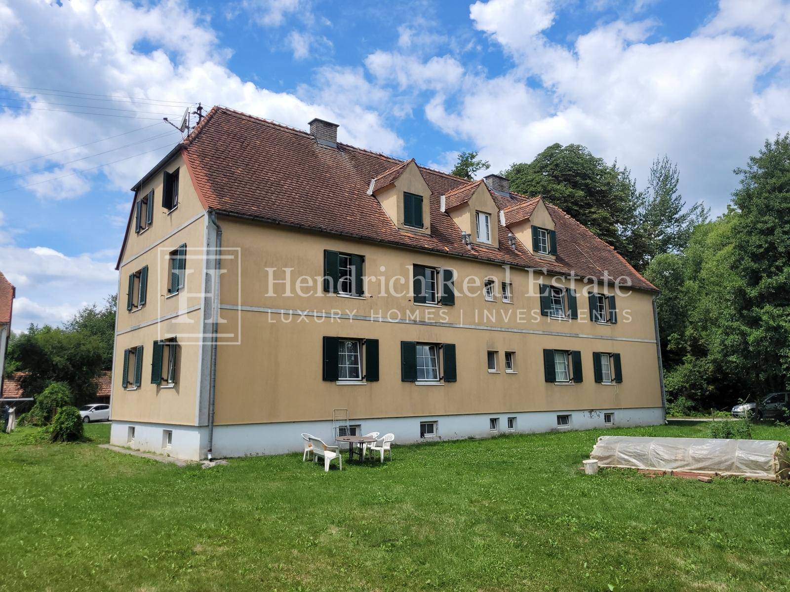 Rückseite des historischen Gebäudes mit großem Garten und Sitzgelegenheiten im Grünen.