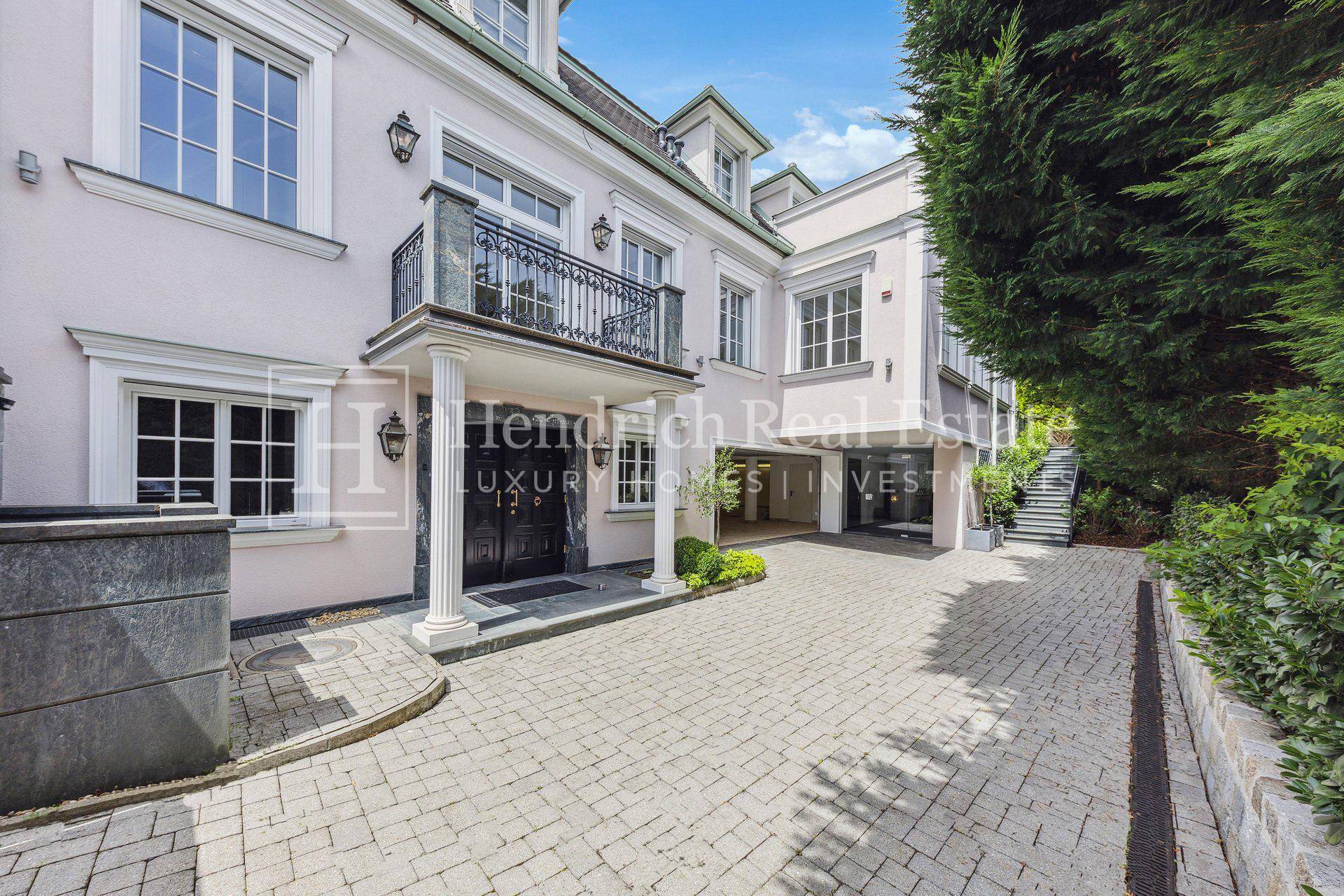 Elegante Fassade der Villa mit Säulen, Balkon und gepflasterter Auffahrt zum Garagenbereich.