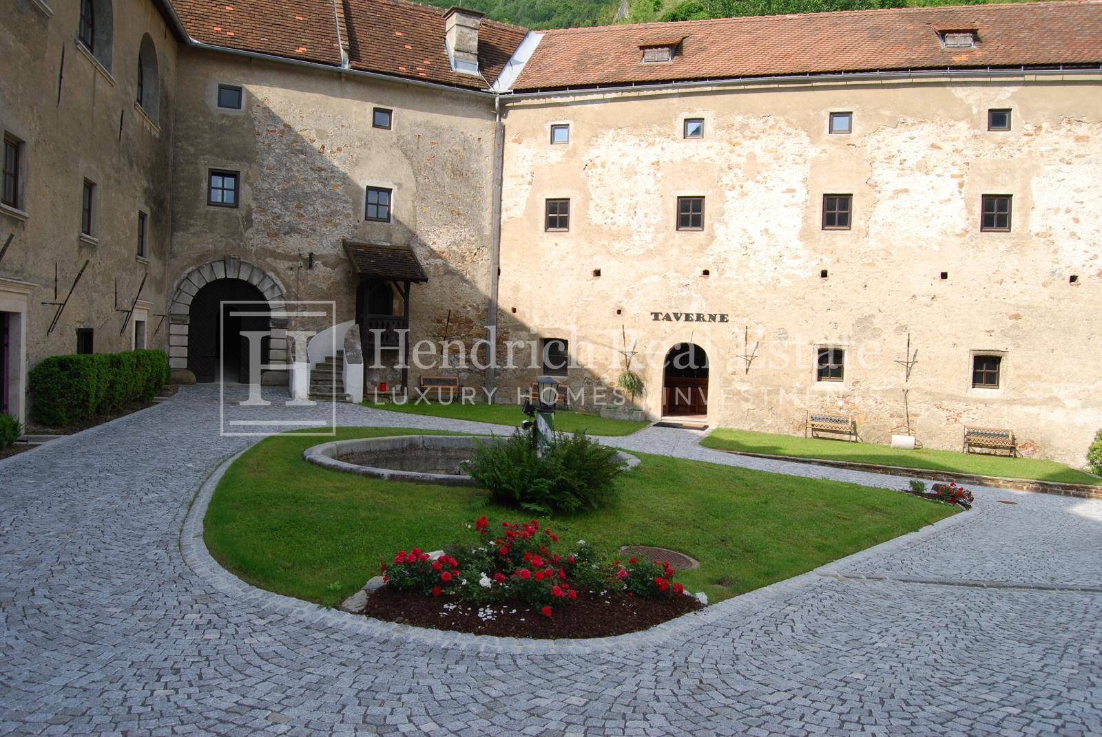 Alter Burghof mit Kopfsteinpflaster, einem kleinen Brunnen und einem Gebäude, das eine Taverne beherbergt.