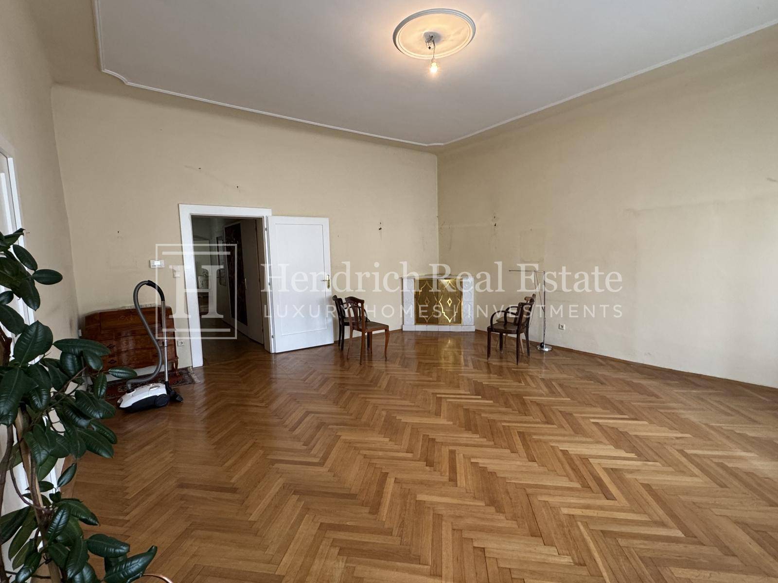 Geräumiges Wohnzimmer mit Fischgrätparkett und hohen Decken, bereit zur Renovierung.