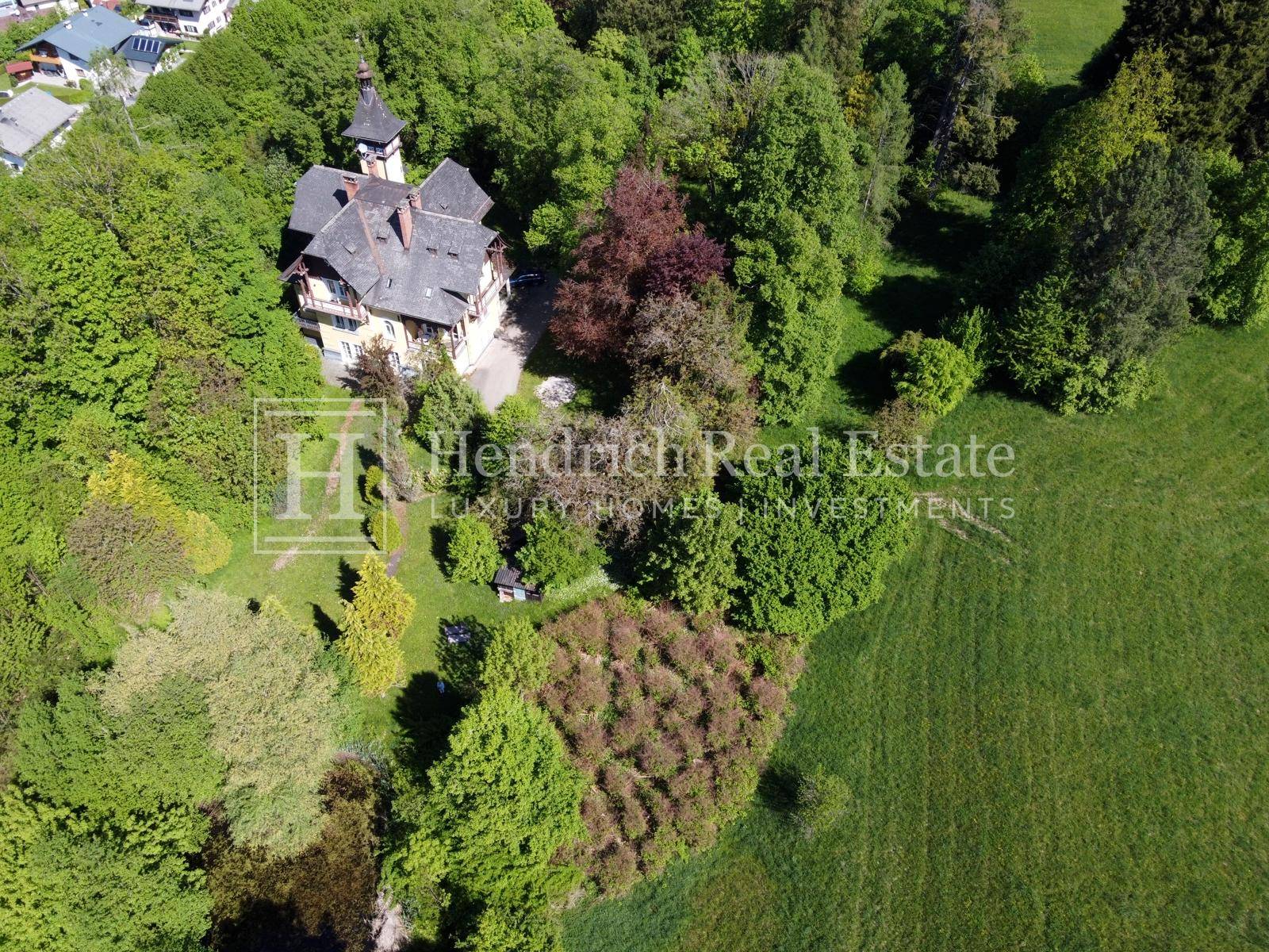 Nahaufnahme der Villa aus der Vogelperspektive, umgeben von dichtem Baumbestand und Grünflächen.