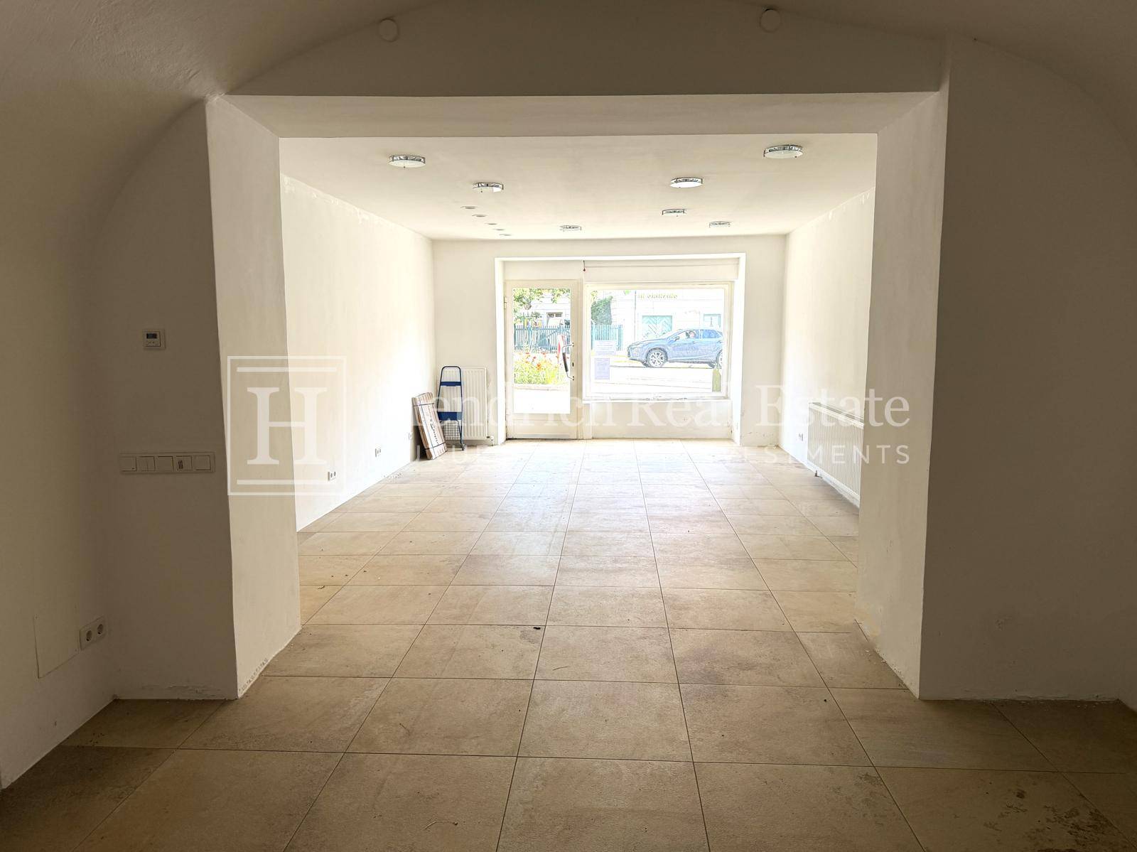 Großer, offener Wohnbereich mit Fliesenboden und gewölbter Decke, mit Blick nach draußen durch eine Glastür.