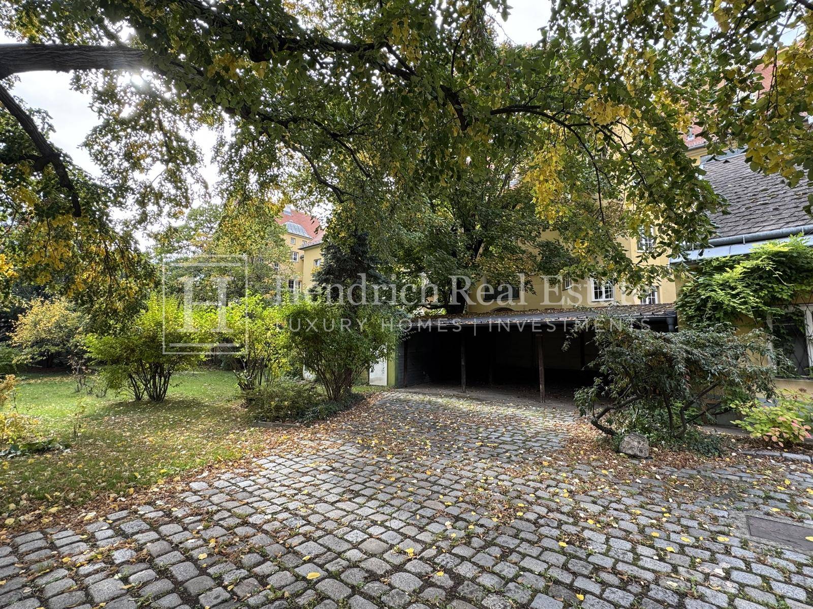 Gepflasterter Hofbereich mit altem Baumbestand und Zugang zu einem Carport.