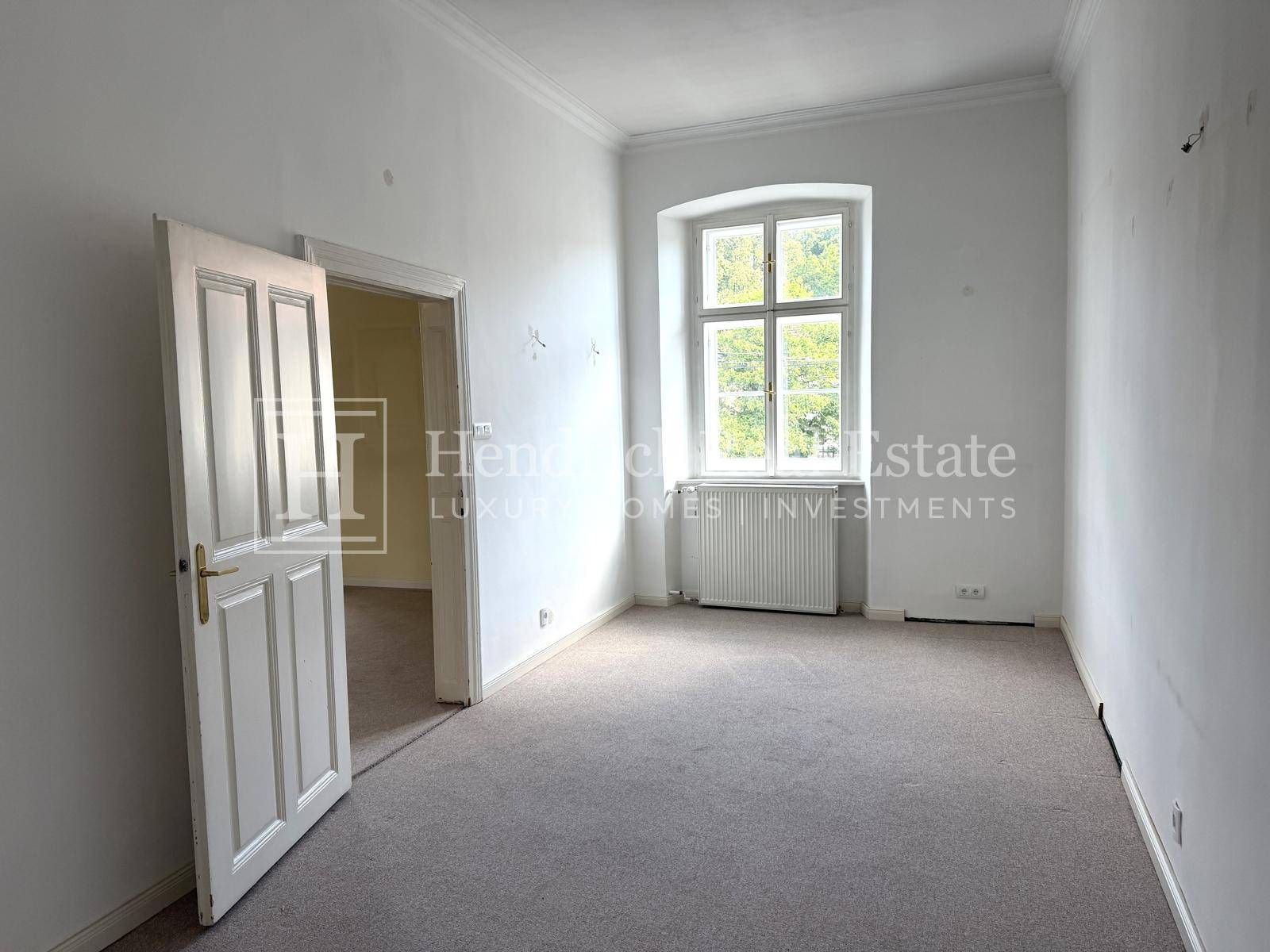 Helles, leeres Zimmer mit Teppichboden und einem Fenster, das viel Tageslicht hereinlässt.