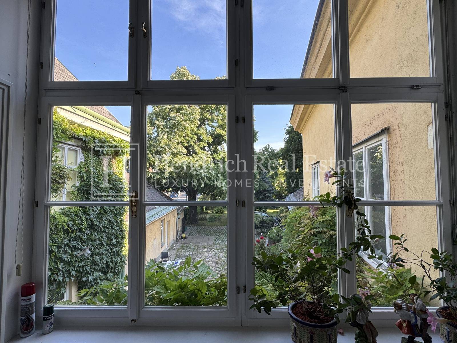 Blick aus einem großen Fenster auf den grünen Innenhof mit historischen Gebäuden.