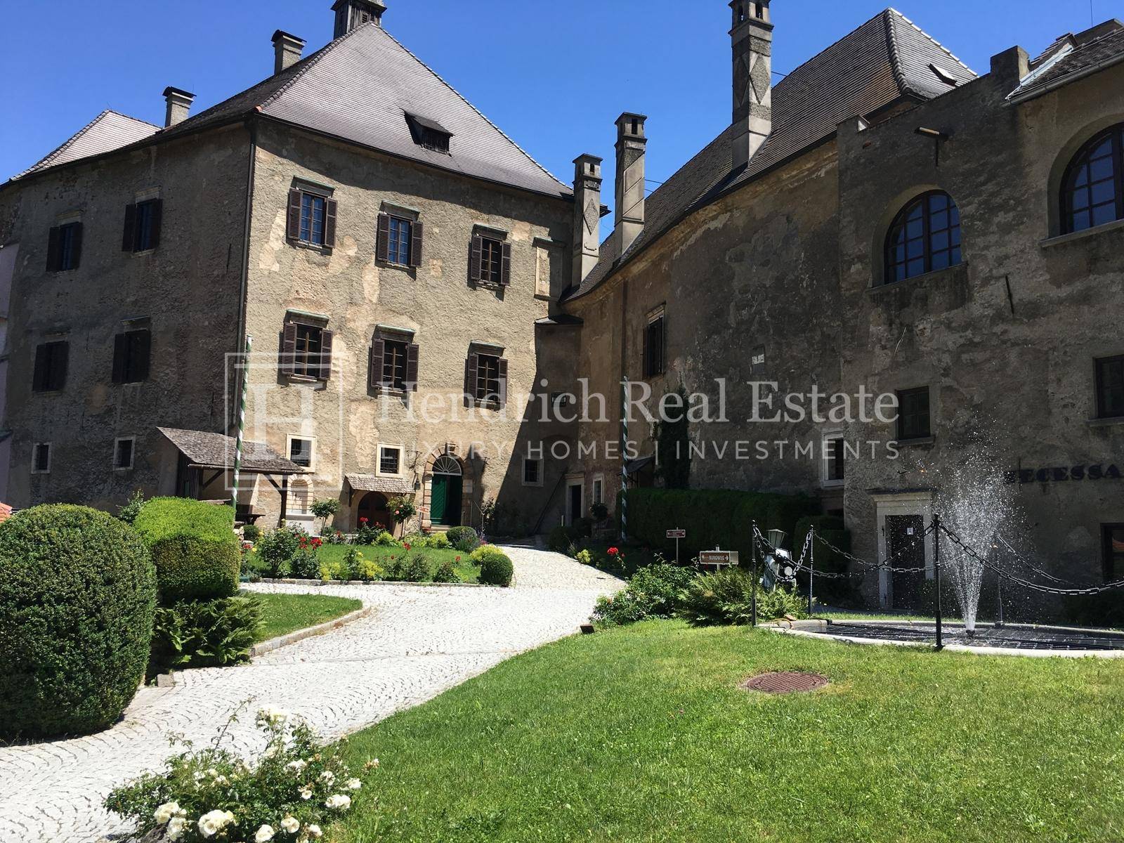 Historischer Innenhof einer Burganlage mit Kopfsteinpflaster, Rasenflächen und einem kleinen Brunnen.