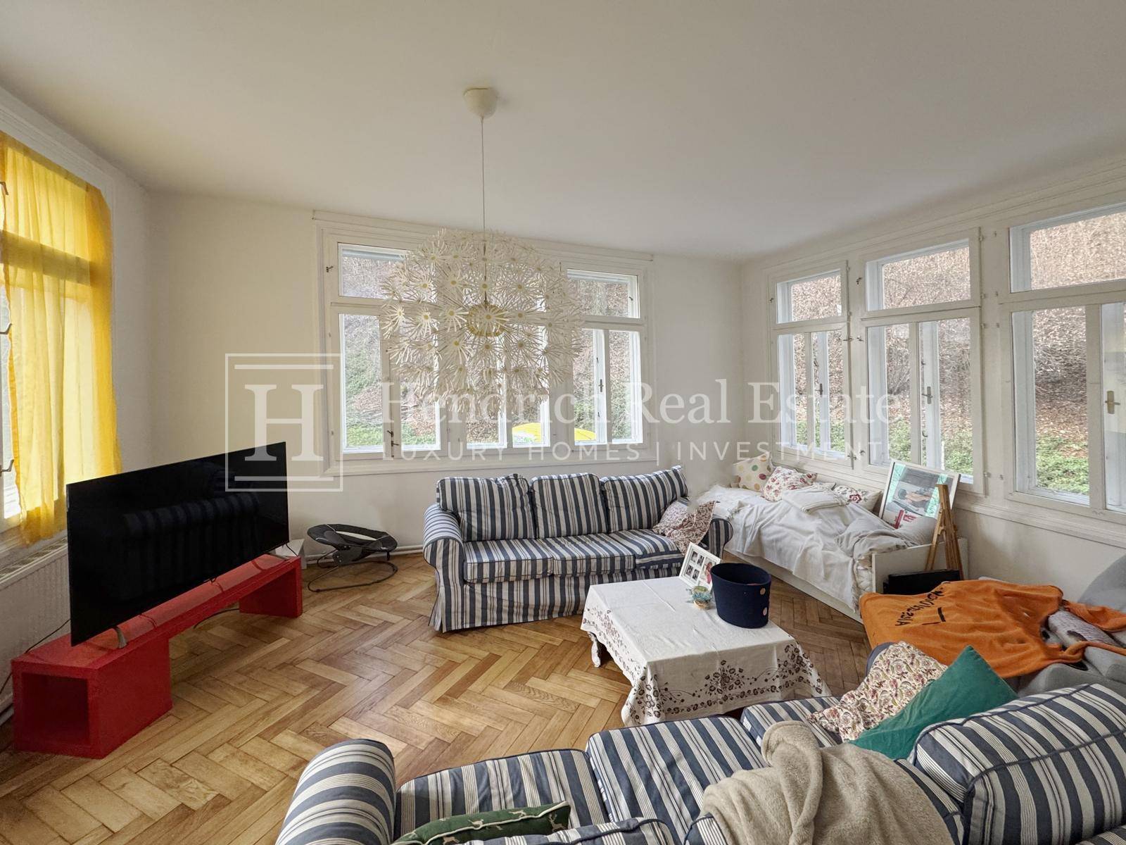Helles Wohnzimmer mit Fischgrätparkett, gestreiften Sofas und großen Fenstern mit Blick ins Grüne.