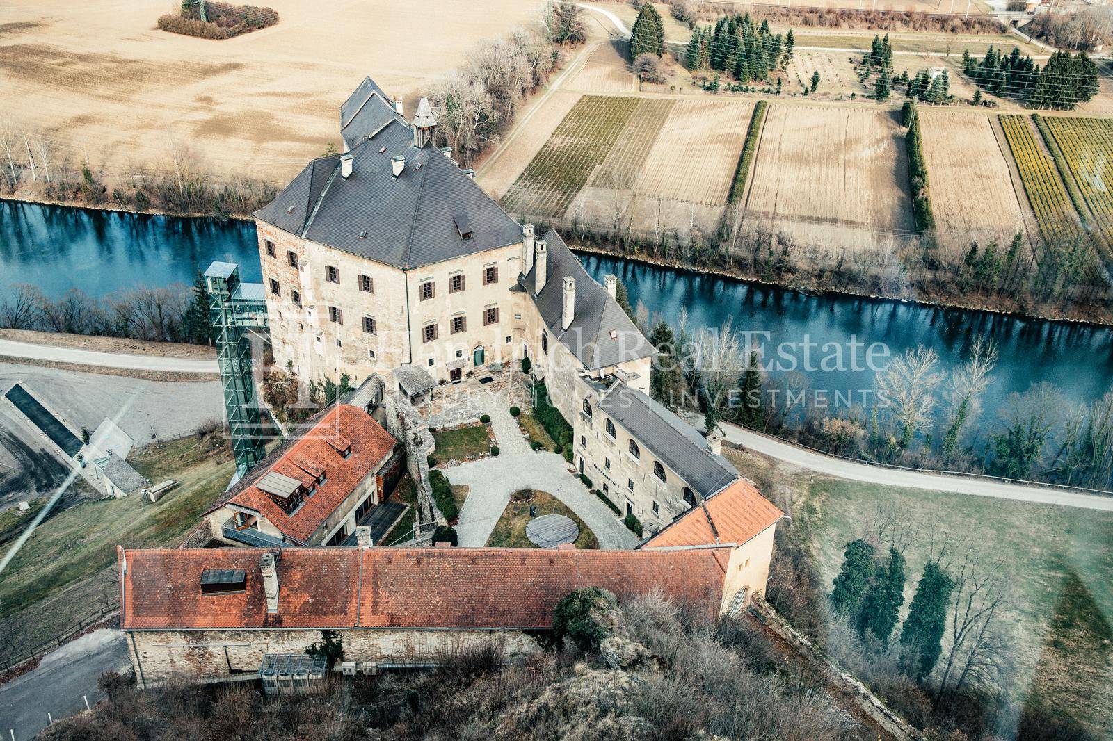 Luftaufnahme des Schlosses am Fluss, umgeben von Feldern und Weinbergen in ländlicher Umgebung.