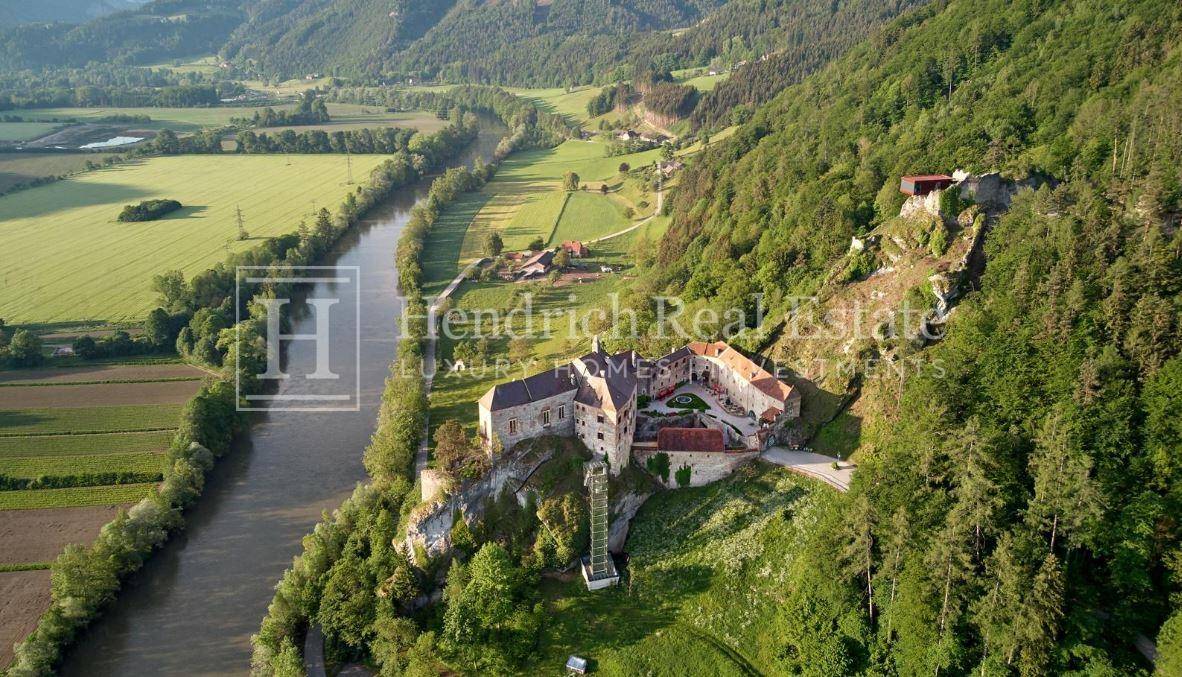 Weitläufige Luftaufnahme der Burganlage am Fluss, eingebettet in eine grüne, ländliche Umgebung.