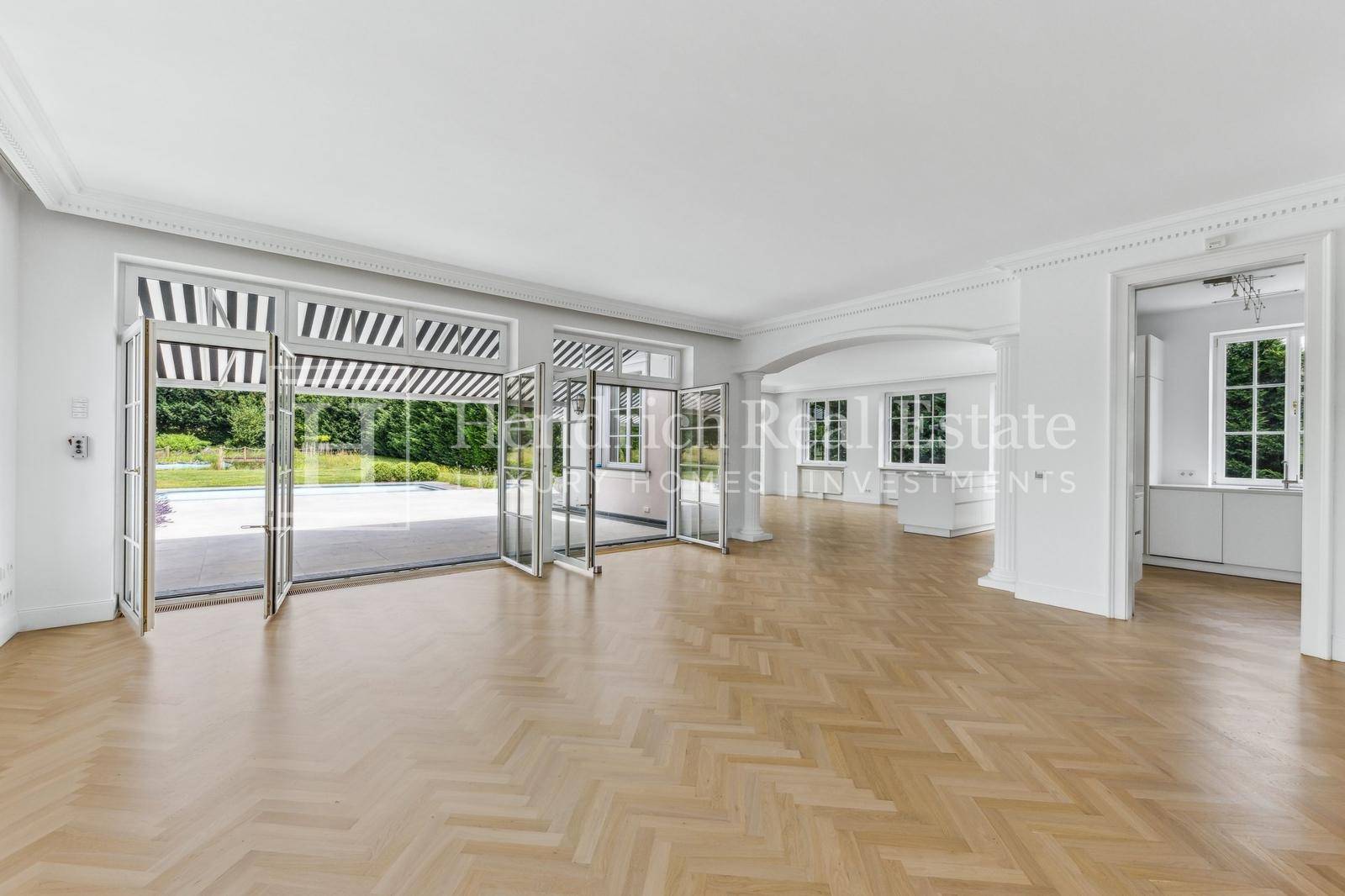 Geräumiges Wohnzimmer mit Fischgrätparkett und großen Fenstertüren zum Poolbereich.