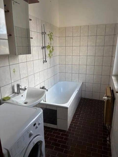 Badezimmer mit Badewanne, Waschbecken, Waschmaschine und hellen Wandfliesen.