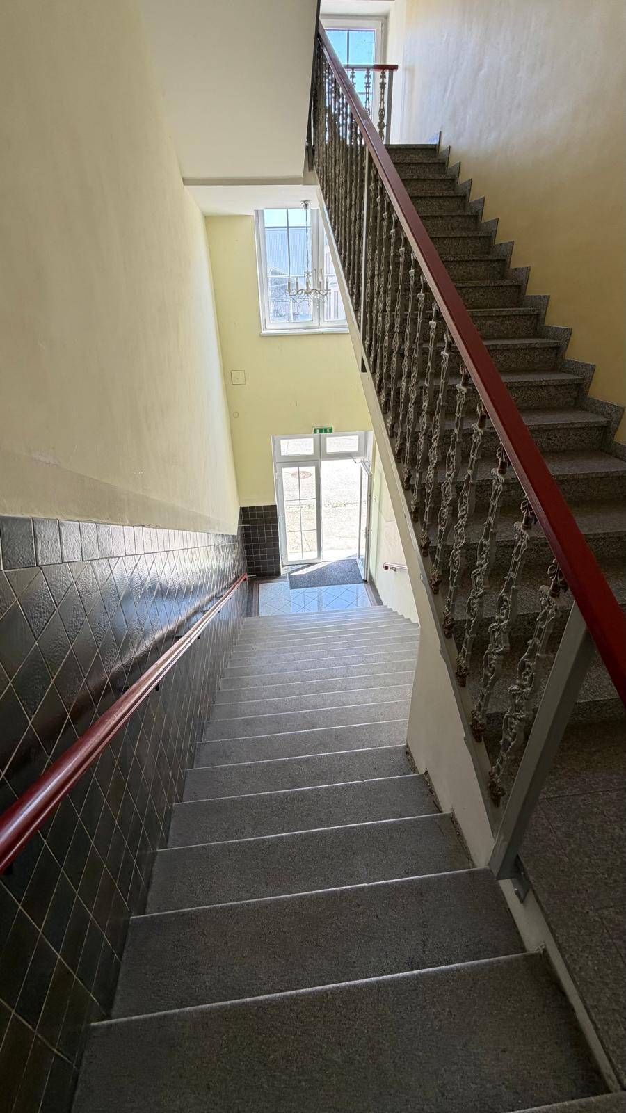 Helles Treppenhaus mit Steinstufen, schmiedeeisernem Geländer und gelben Wänden.