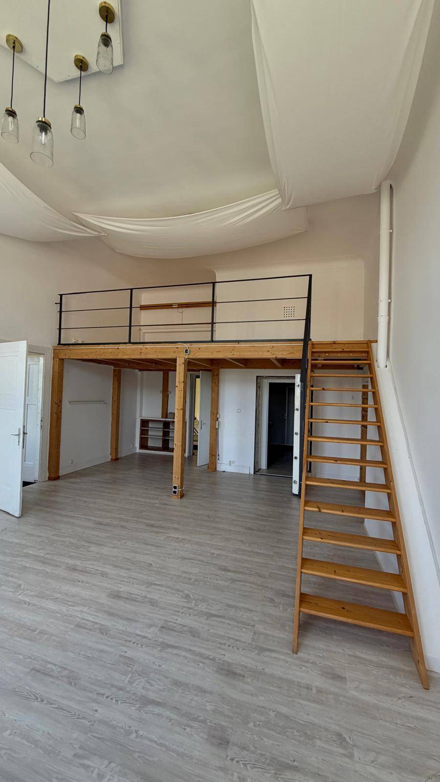 Heller Wohnbereich mit hoher Decke, einer Holzempore und einer Treppe, die nach oben führt.