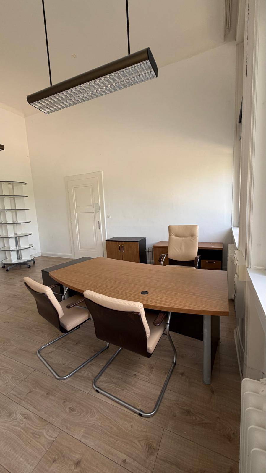 Helles Büro mit modernem Schreibtisch, Bürostühlen und hohen Fenstern, die den Raum mit viel Tageslicht versorgen.