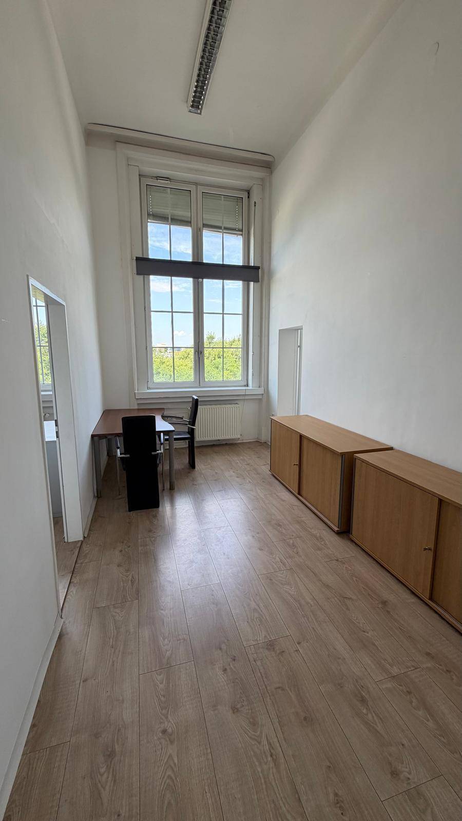 Langes, schmales Büro mit Laminatboden, einem Fenster und Holzschränken entlang der Wand, bietet viel Stauraum.