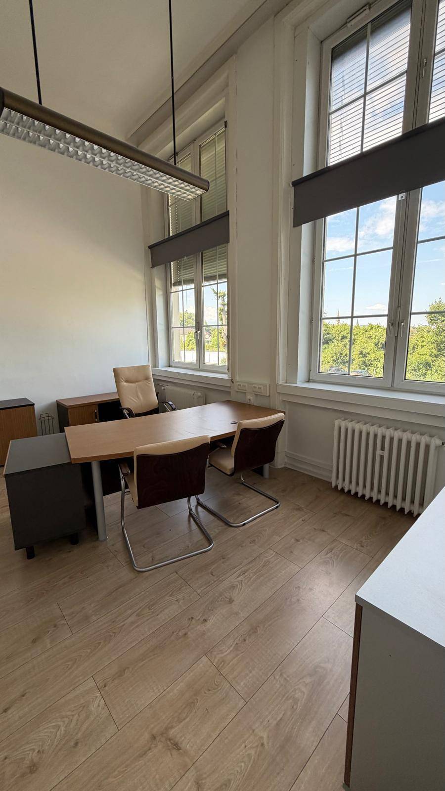 Büro mit hellem Laminatboden, modernen Büromöbeln und großen Fenstern, die den Raum mit Tageslicht durchfluten.