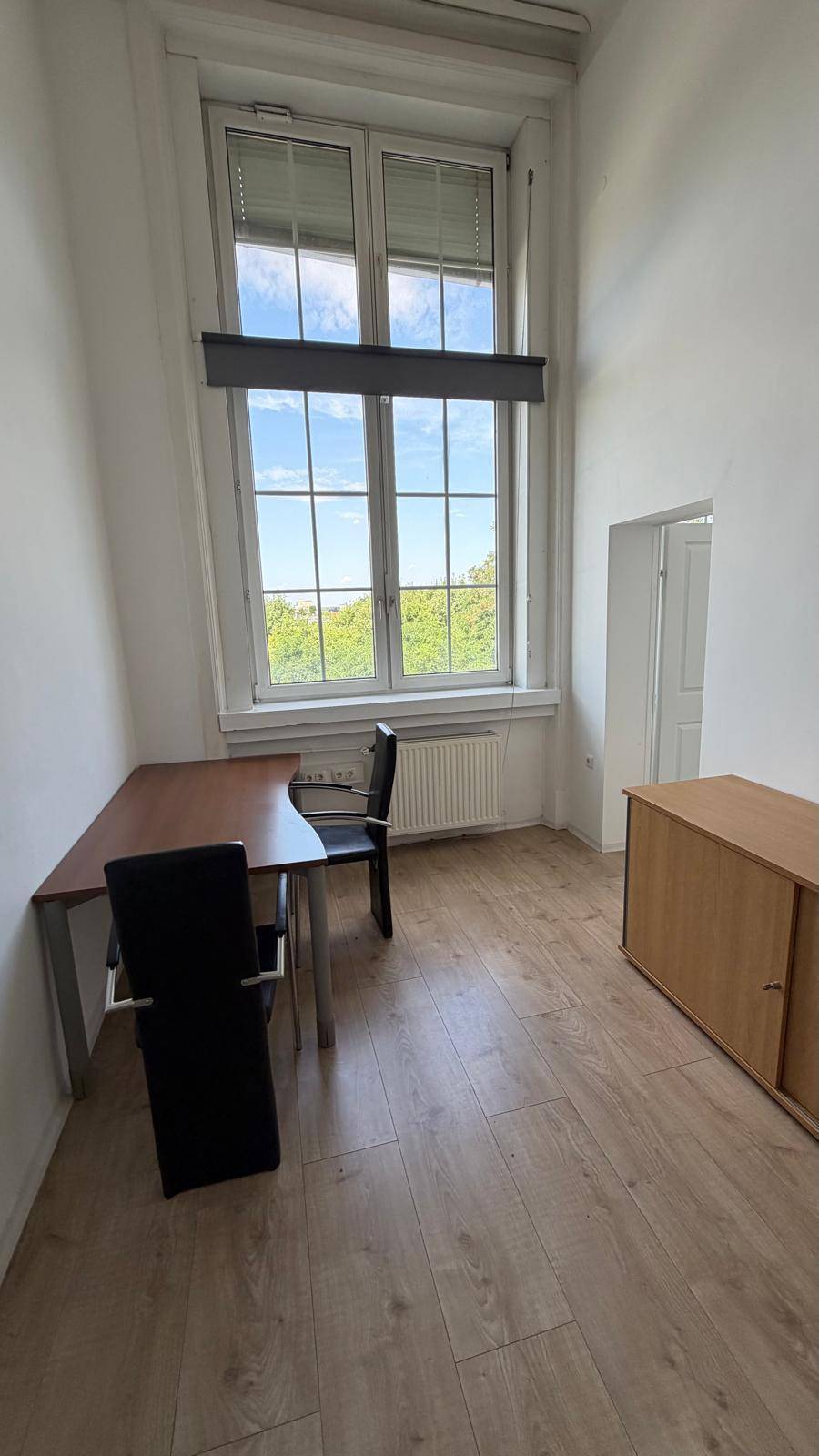 Büro mit Laminatboden, einem Schreibtisch und einem großen Fenster mit Blick ins Grüne, bietet eine ruhige Arbeitsumgebung.