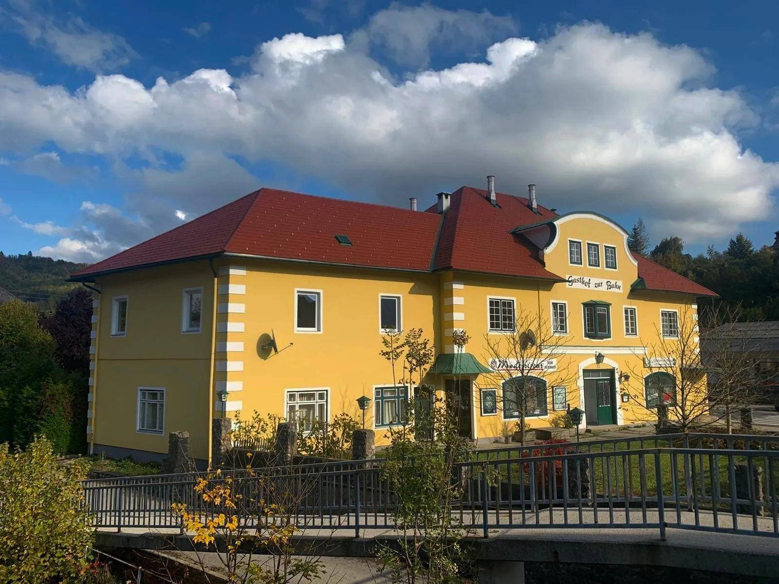 Traditionelles gelbes Gebäude mit rotem Dach und Brücke im Vordergrund unter blauem Himmel.
