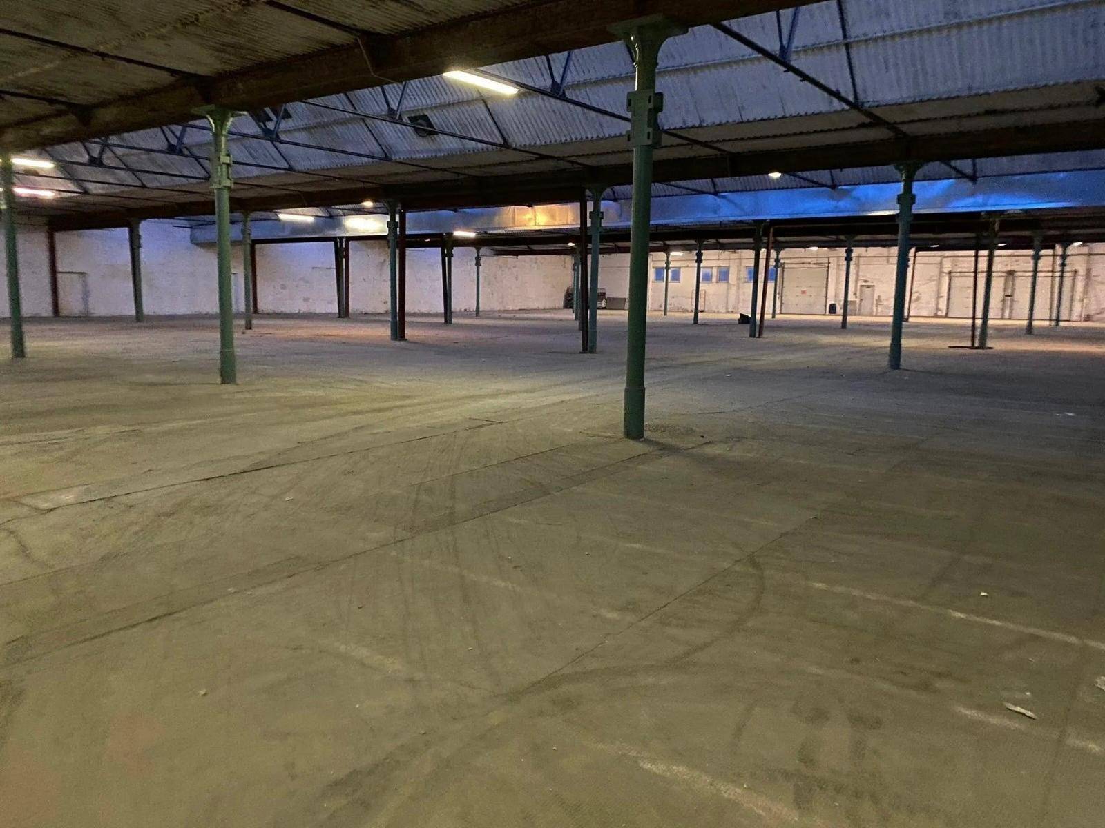 Geräumige, leere Industriehalle mit Betonboden, grünen Stützpfeilern und sichtbarer Dachkonstruktion.