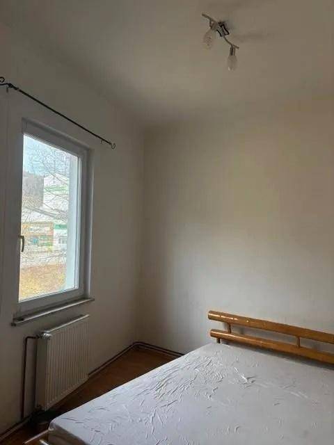 Helles Schlafzimmer mit einfachem Bettgestell, Fenster und Heizkörper, bereit zur Einrichtung.