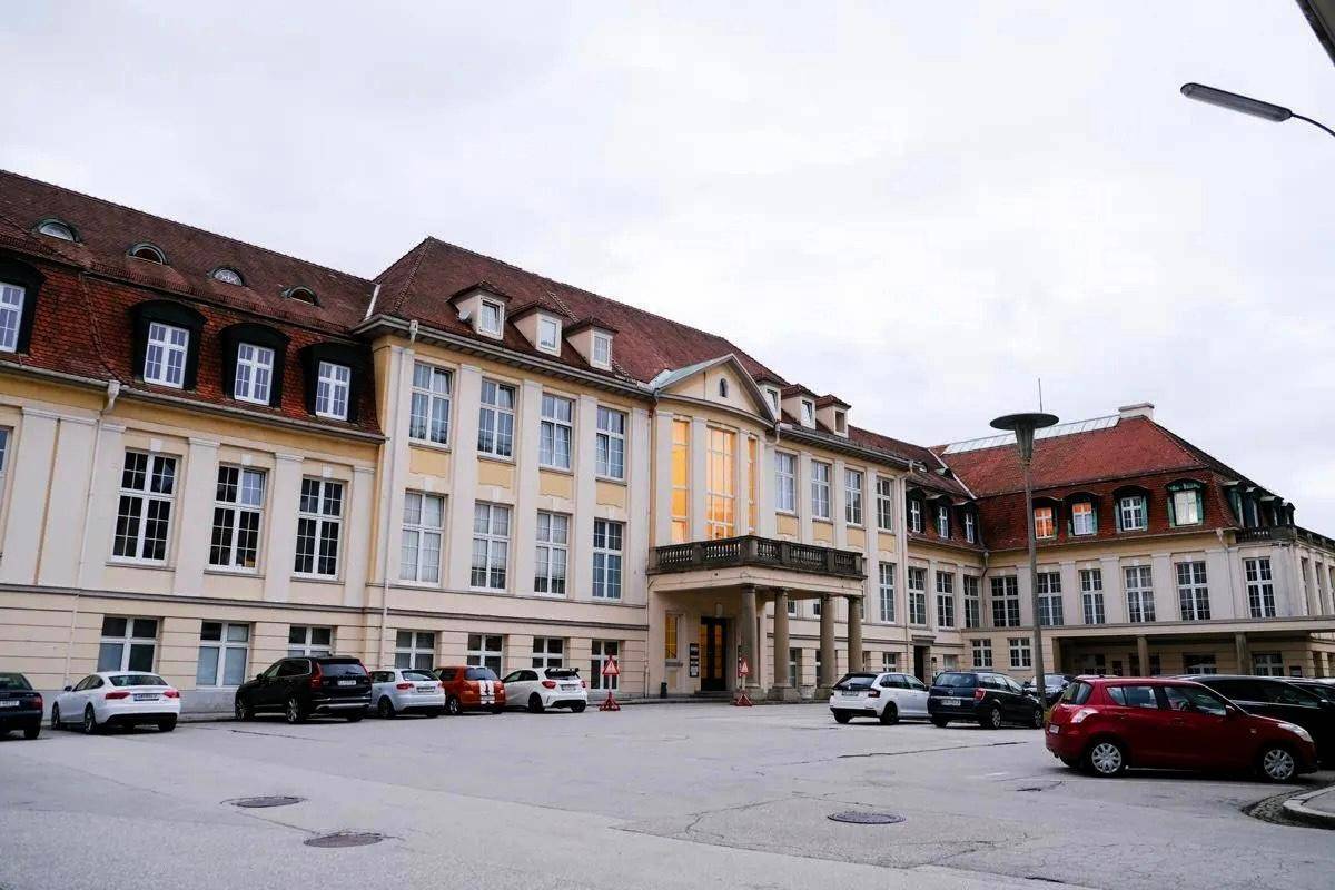 Großes, historisches Gebäude mit rotem Dach und vielen Fenstern, umgeben von einem Parkplatz.