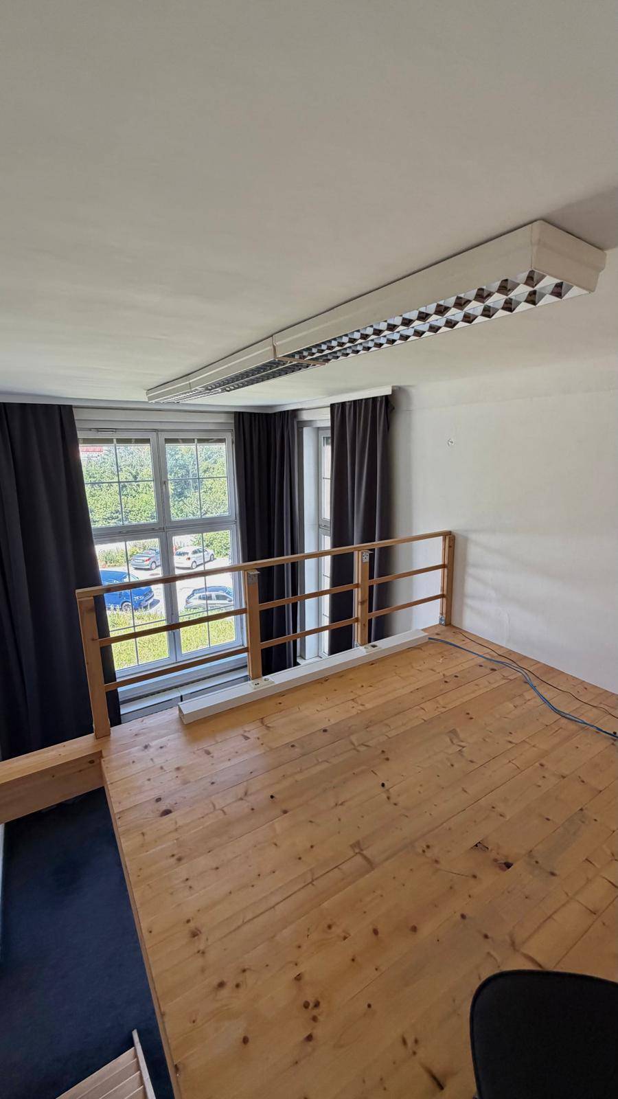 Obere Empore mit Holzdielenboden und Blick auf die Fenster mit dunklen Vorhängen.