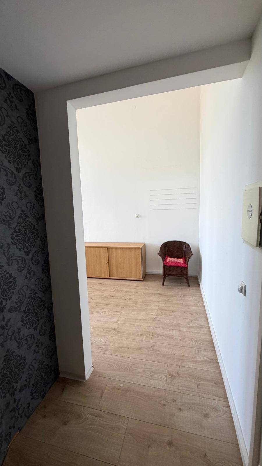 Flur mit gemusterter Tapete und Blick in einen hellen Raum mit Laminatboden und Holzschrank, einladend gestaltet.