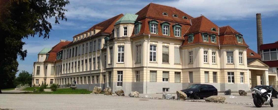 Weitläufige Außenansicht des historischen Gebäudes mit rotem Dach und blauer Himmelkulisse.
