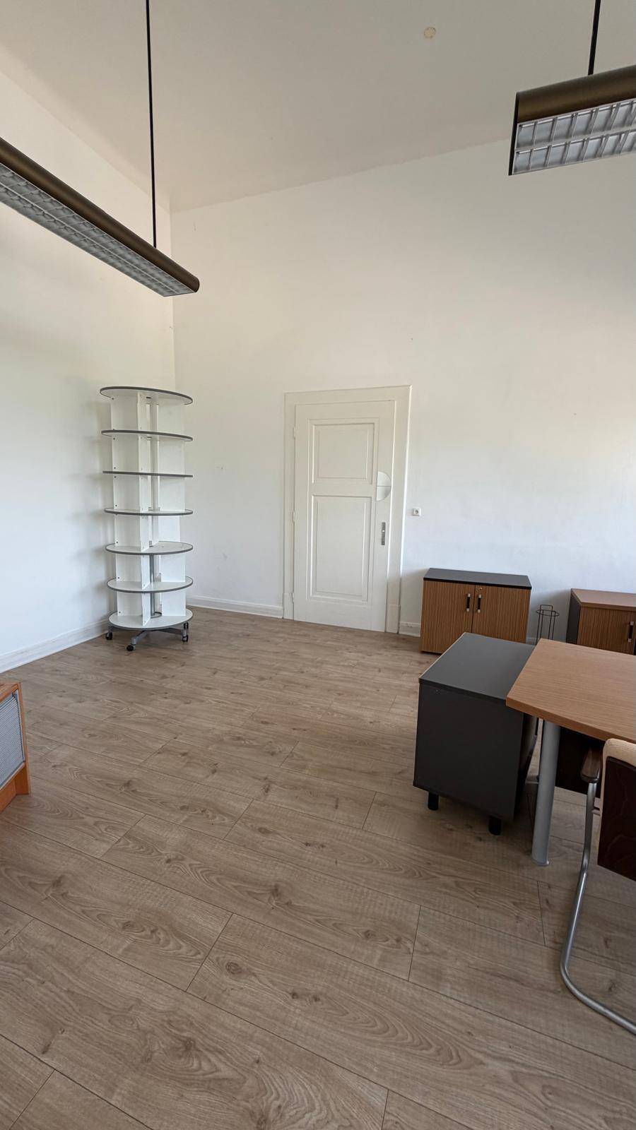 Geräumiges Büro mit Laminatboden, einer weißen Tür und einem runden Regal im Hintergrund, bietet viel Platz.
