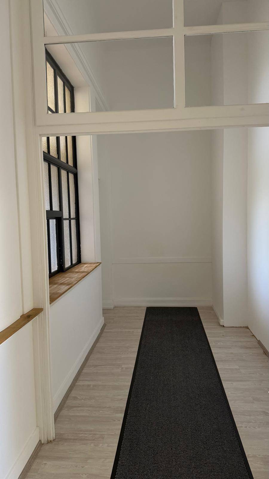 Langer Flur mit hellem Laminatboden und einem großen Fenster mit Sprossen, das Licht spendet.