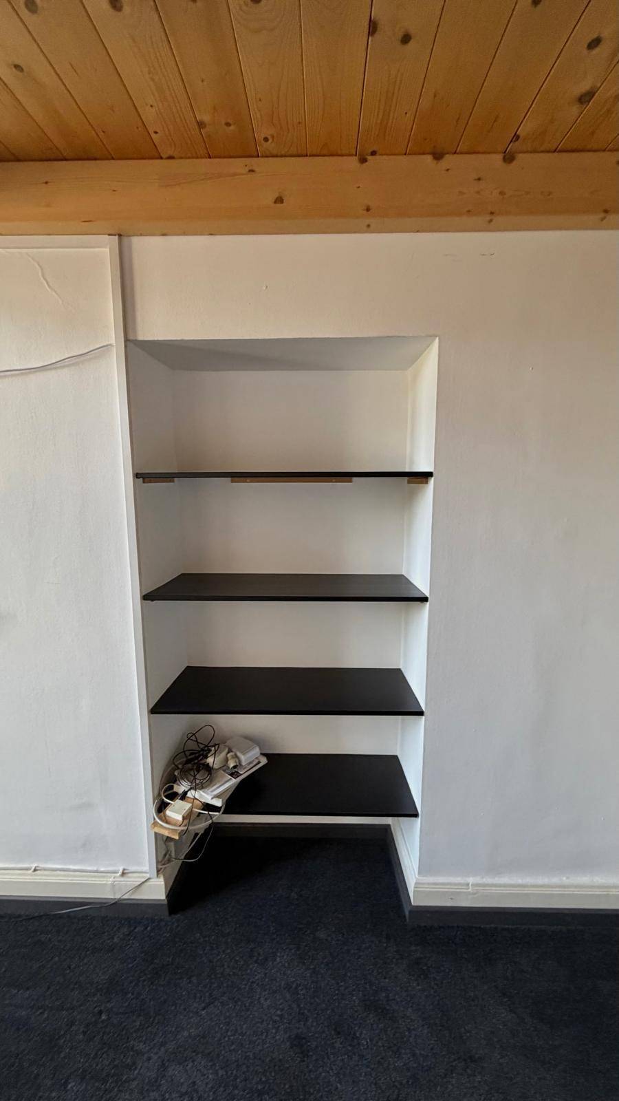 Eingebaute Regale mit schwarzen Ablagen in einer Nische, ideal für Stauraum und Dekoration.