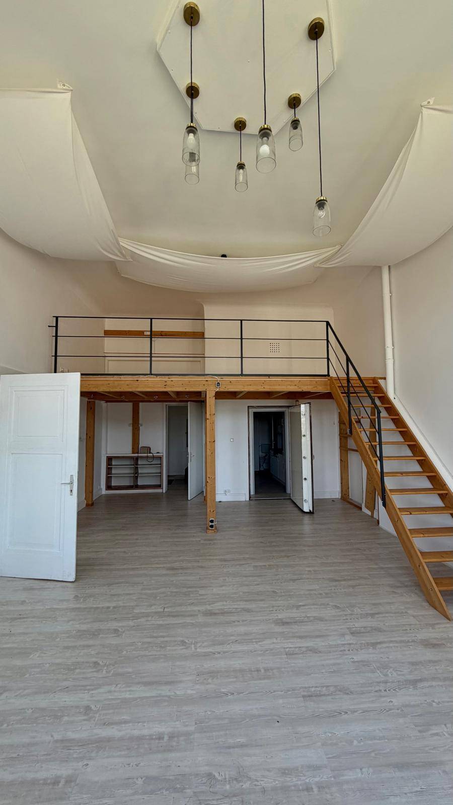 Geräumiger Wohnbereich mit hoher Decke, einer Holzempore und einer Treppe, die nach oben führt.