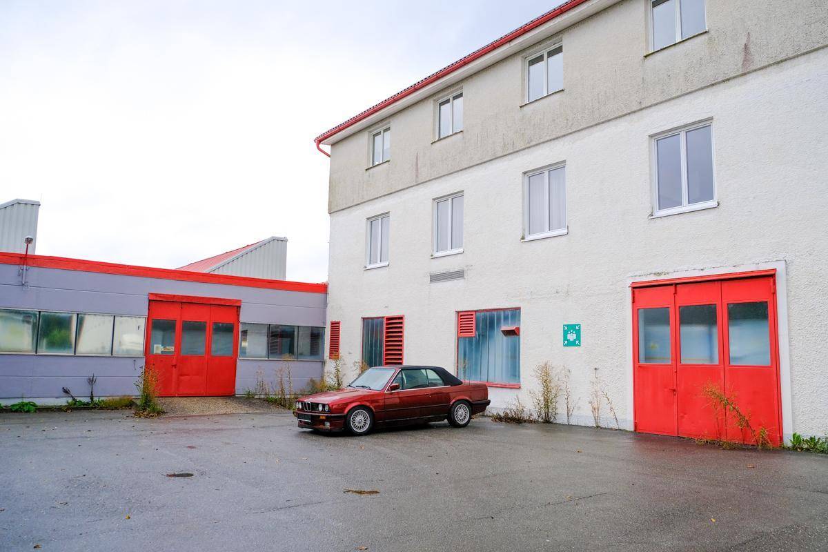 Gewerbegebäude mit weißer Fassade und roten Türen, davor ein rotes Auto auf dem asphaltierten Vorplatz.