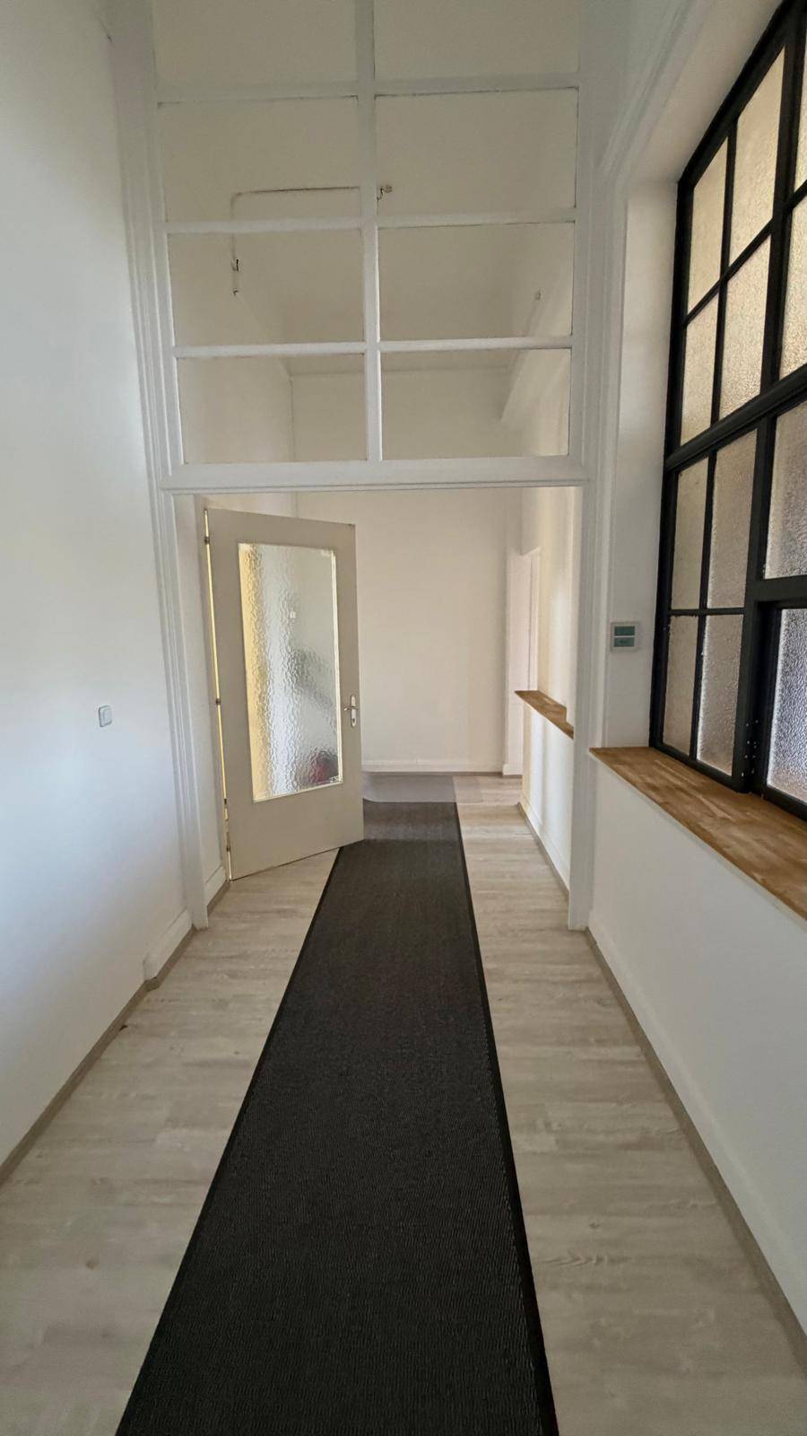 Heller Flur mit Laminatboden, einem großen Fenster und einer Tür mit Glaseinsatz.