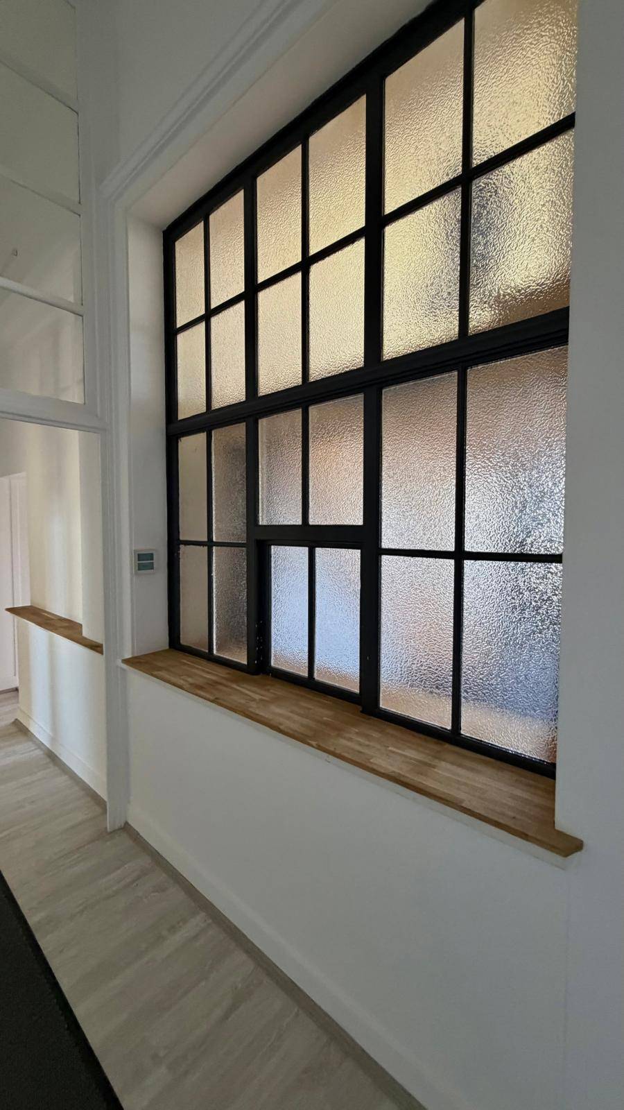 Langer Flur mit einem großen Fenster mit schwarzem Rahmen und strukturiertem Glas.