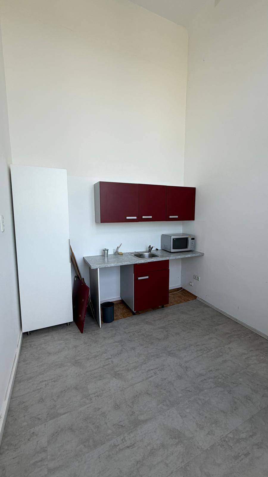 Kleine Küchenzeile mit roten Hängeschränken, Spüle und Mikrowelle in einem hellen Raum, inklusive Kühlschrank.